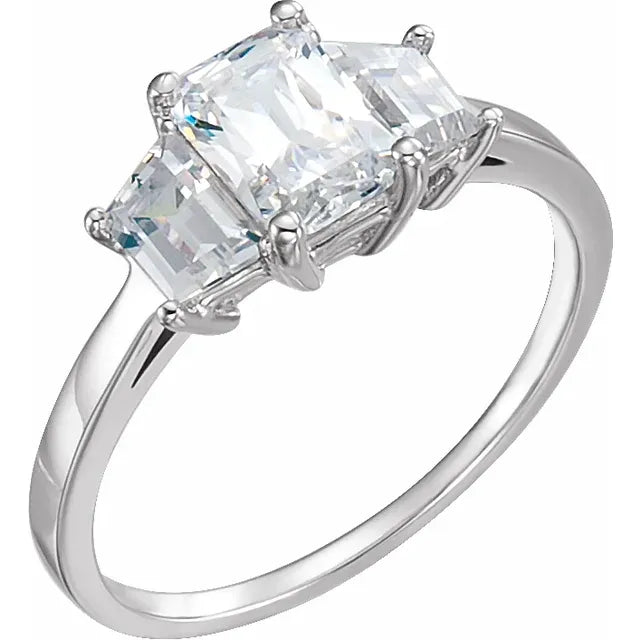 An image showing a white gold 3-stone engagement ring with an emerald shaped center diamond flanked by trapezoid shaped diamonds on each side