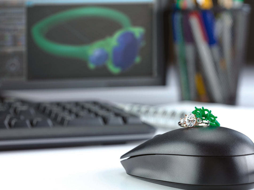 A finished engagement ring next to it's wax model in front of a computer showing the digital design of the ring