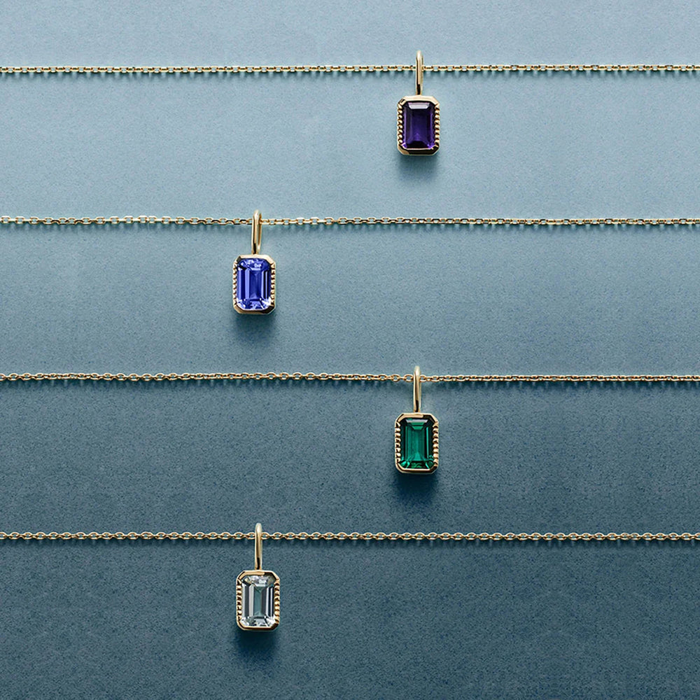 Four 14K yellow gold emerald-cut gemstone pendant necklaces laid flat, including the lab grown aquamarine style | AJ's Jewelry