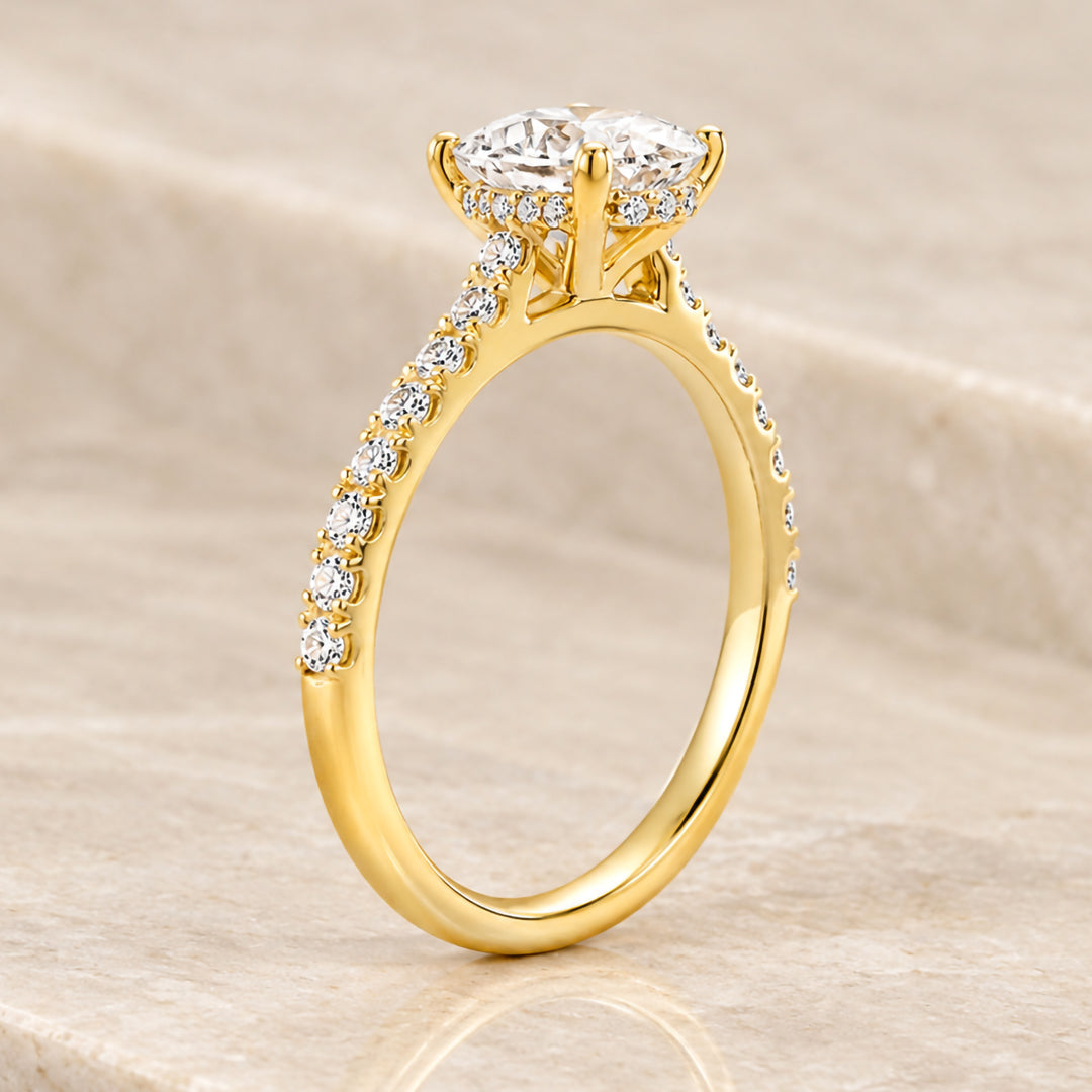 18 karat yellow gold 2ct oval lab grown diamond hidden halo engagement ring with diamond accent band shown from the side on a styled display at AJ's Jewelry in Ridgewood, Queens NY