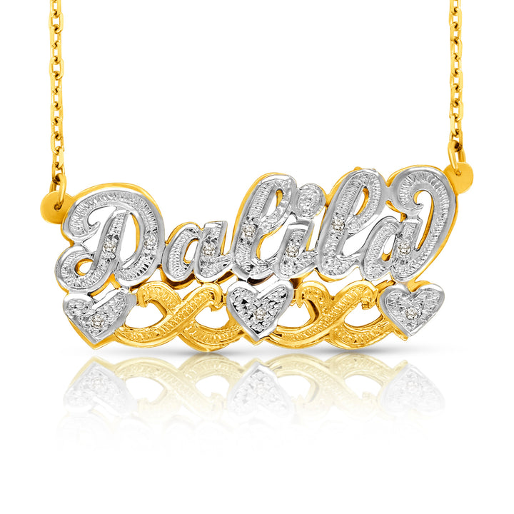 A custom name necklace featuring the name 'Dalia' in cursive script, embellished with small clear stones, with three heart-shaped accents. The necklace is made of yellow gold and white gold, suspended from a gold chain against a white background with a soft reflection below.