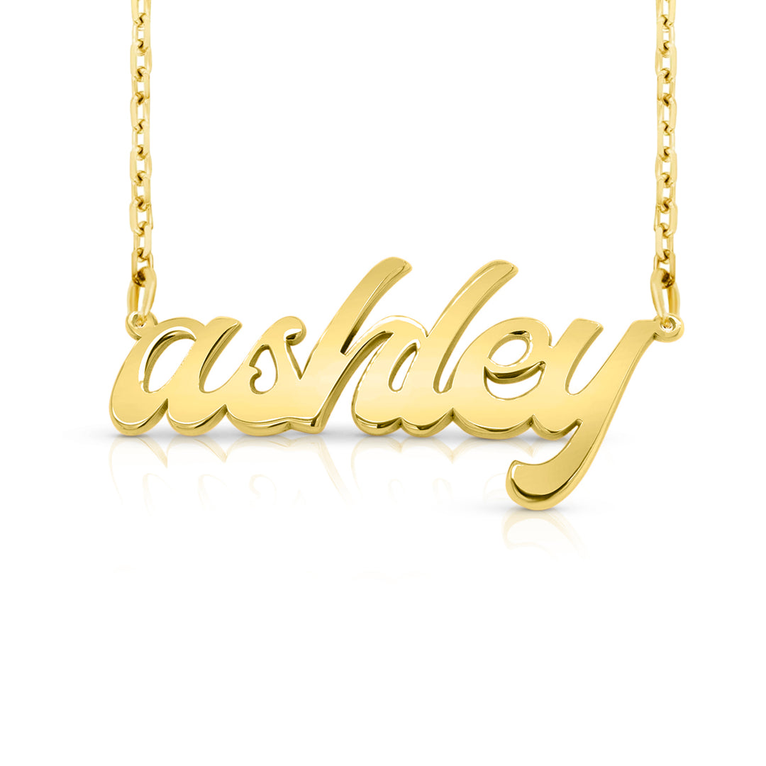 A gold nameplate necklace spelling 'ashley' in cursive script, suspended from a delicate gold chain against a clean white background. This photo can change appearance depending on the name input using the custom name builder