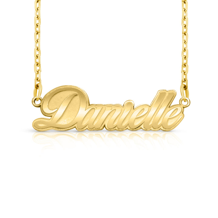 A gold nameplate necklace spelling 'Danielle' in cursive script, suspended from a delicate gold chain against a white background with a soft reflection below.  This photo can change appearance depending on the name input using the custom name builder