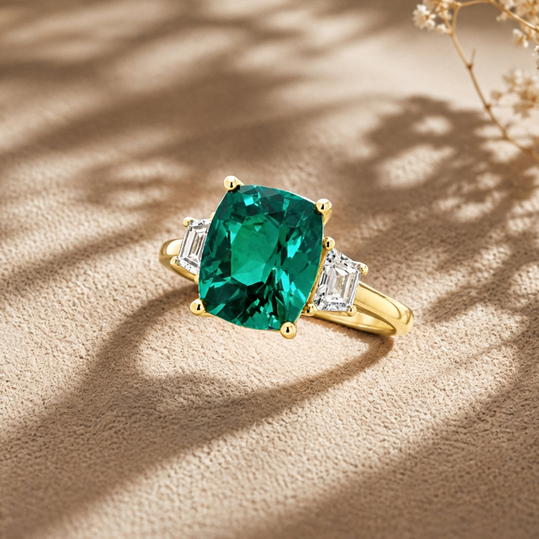 Custom 14KT yellow gold lab-grown emerald three-stone ring with matching band shown at an angle on a styled display at AJ's Jewelry in Ridgewood, Queens NY
