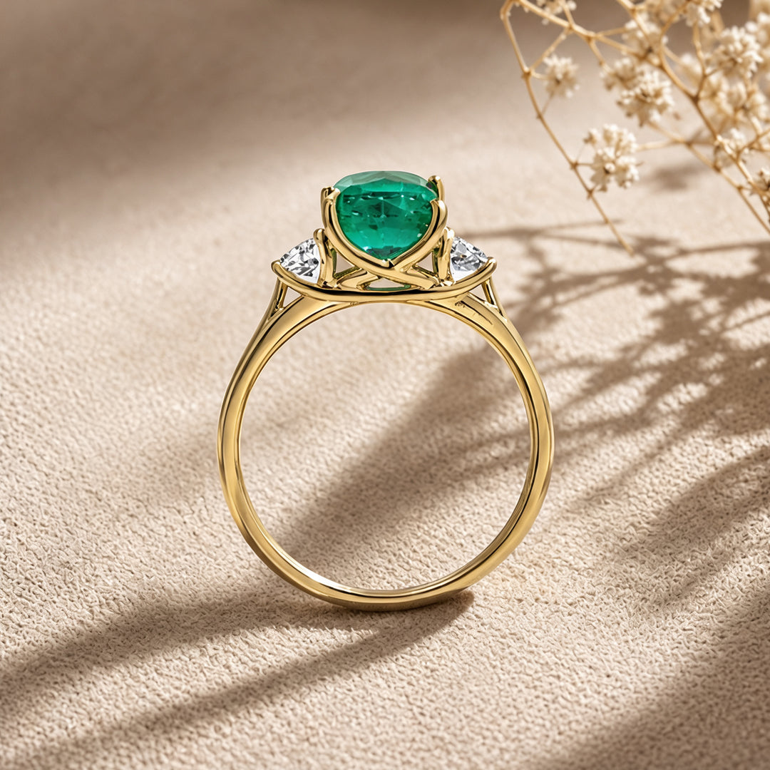 Custom 14KT yellow gold lab-grown emerald three-stone ring with matching band shown from the side on a styled display at AJ's Jewelry in Ridgewood, Queens NY